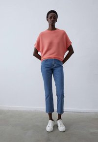 Koralų juostelėmis dekoruota trumpomis rankovėmis palaidinė, derinama su šviesiai mėlynomis trumpomis džinsinėmis kelnėmis ir baltais sportbačiais; smooth texture, relaxed fit, minimal seams.