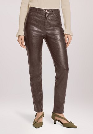 Femme portant un pantalon en cuir marron foncé associé à un pull côtelé crème et des escarpins verts olive à bout pointu avec des brides.