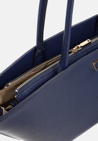 Navyblaue Handtasche mit strukturiertem Design, doppelten Griffen, Reißverschluss und goldenen Hardware-Akzenten. Sie verfügt über ein geteiltes Innenfach mit Reißverschlusstaschen.