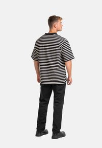 Camisa de manga corta a rayas en negro y crema, con un ajuste relajado. Combinada con pantalones negros y zapatos negros gruesos, vista desde la espalda.