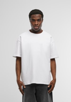 Weißes Baumwoll-T-Shirt mit lockerer Passform, kurzen Ärmeln und Rundhalsausschnitt, kombiniert mit dunkelgrauen Jeans. Einfaches, einfarbiges Design.