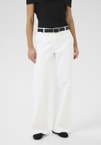 Witte wijde broek met zakken aan de voorkant, voorzien van een zwarte riem met een zilveren gesp. Gepaard met een zwarte off-the-shoulder top.