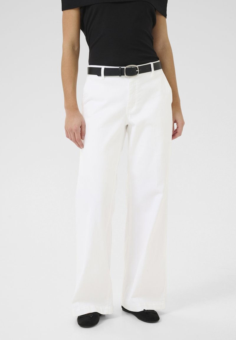 Witte wijde broek met zakken aan de voorkant, voorzien van een zwarte riem met een zilveren gesp. Gepaard met een zwarte off-the-shoulder top.