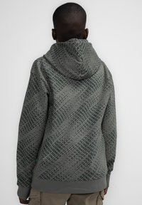 Felpa grigia con cappuccio caratterizzata da un motivo in verde scuro, maniche lunghe e polsini e orlo a costine. Tessuto texturizzato visibile.