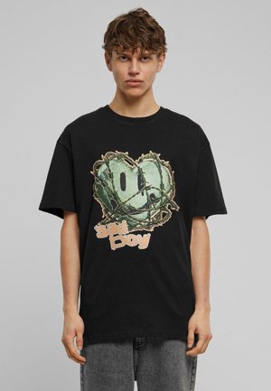 Sort bomulds t-shirt med et grafisk design af et grønt smilende ansigt indviklet i pigtråd og ordene "sad boy" i lys beige.