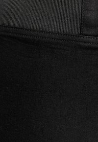 Svart atletisk plagg med en strukturerad tygkvalitet och en slät yta, ribbad midja och rena sömmar längs kanterna.