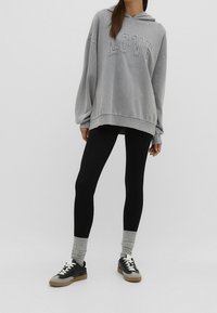 Felpa oversize grigia con la scritta "LOVE", abbinata a leggings neri e calzini con accenti grigi. Indossata con sneakers nere e grigie.