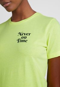 Koszulka bawełniana w neonowym zielonym kolorze z czarnym napisem "Nigdy na czas", okrągłym dekoltem i krótkimi rękawami. Miękka tekstura, swobodny krój.