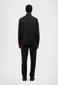 Zwarte lange mouwen shirt en broek, beide in een gladde, matte stof. Het shirt heeft een puntkraag en knoopmanchetten.
