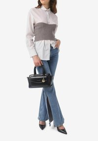 Borsa nera con accessori in oro, corsetto grigio a righe sopra una camicia bianca, jeans a vita alta azzurri svasati e décolleté neri con punta.
