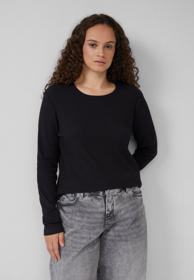 Schwarzes Langarmshirt mit geripptem Stoff, rundem Ausschnitt und leicht verkürztem Schnitt, kombiniert mit hellgrauen, locker sitzenden Jeans.