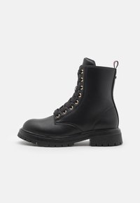 Stivale da combattimento in pelle nera con occhielli dorati, punta rotonda, suola robusta e design con lacci. Presenta un'etichetta sul retro.