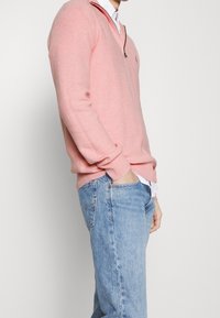 Ljusrosa stickad tröja med halvdragkedja, bärs över en vit skjorta, ihop med ljusblå denimjeans. Strukturerad tyg.