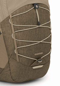Sac à dos en tissu marron avec une surface texturée, doté d'un système de cordon élastique beige et d'un logo discret "QUASAR" sur le côté.