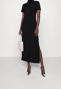 Musta istuva mekko korkealla kauluksella, lyhyillä hihoilla, sivupilkulla ja nappi-yksityiskohdilla. Yhdistetty fringekäsilaukkuun ja metallinkimalteisiin kenkiin.