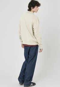 Un pull cr�ème à col, associé à un pantalon à rayures navy décontracté et des chaussures noires.