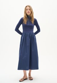 Rochie lungă de culoare bleumarin, cu un top ajustat din material ribbat și fustă plisată, având un fermoar pe jumătate la gât. Material neted, design lungime până la gleznă.