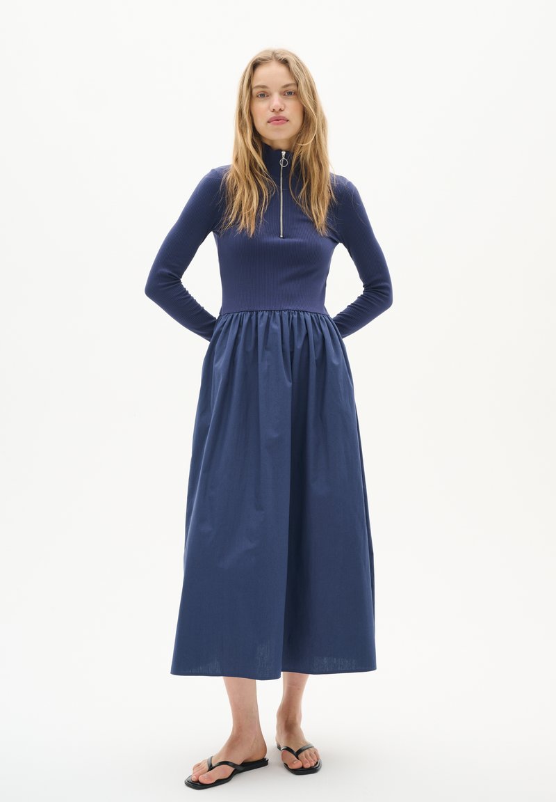 Rochie lungă de culoare bleumarin, cu un top ajustat din material ribbat și fustă plisată, având un fermoar pe jumătate la gât. Material neted, design lungime până la gleznă.