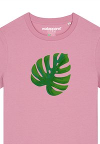 Roze t-shirt met korte mouwen met een grote groene monstera bladafbeelding. Gemaakt van zacht katoen. Label zegt "wat apparel."