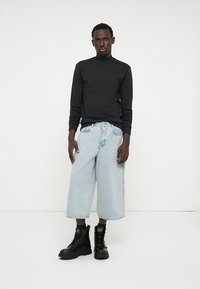 Top nero a maniche lunghe, jeans a gamba larga di un blu chiaro e stivaletti combat neri con suola spessa. Design semplice senza motivi o loghi visibili.