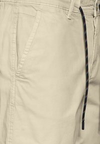 Beżowe szorty wykonane z lekkiego materiału, o gładkiej fakturze, z bocznymi kieszeniami oraz czarnym sznurkiem do ściągania z czerwonymi i niebieskimi akcentami.