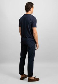 Tricou din bumbac bleumarin cu mâneci scurte, asortat cu pantaloni închiși la culoare și pantofi de bărbați din piele maro, tip barcă. Design simplu pe spate, siluetă ajustată.