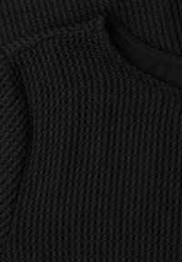 Tissu noir avec un motif en maille gaufrée texturée et un col rond avec une doublure intérieure lisse visible.