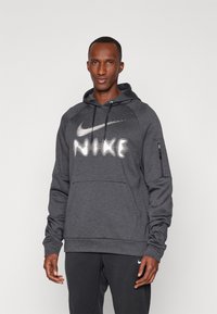 Tmavošedá mikina Nike s predným klokaním vreckom, bielym logom, kapucňou so šnúrkou a zipsovým vreckom na rukáve na ukladanie vecí.