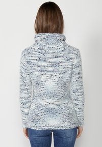 Långärmad, vit och blåmelerad tröja med hög krage, mjukt material och en figursydd silhuett som sträcker sig ner till en utsvängd nederkant.