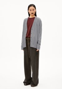 Gray cardigan with buttons, textured fabric, worn over a maroon shirt. Paired with loose, dark brown trousers and black shoes.