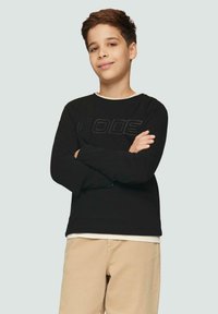 Schwarzes Langarmshirt mit strukturiertem "CODE"-Grafik, cremefarbenem Kragen und beigen Hosen. Glattes Material mit eng sitzenden Ärmeln.