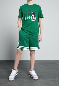 Zielona koszulka z nadrukiem "23 JORDAN", zestawiona z zielonymi szortami z białymi paskami i kropkami. Białe trampki z zielonymi akcentami.