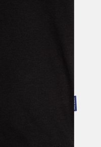 Tissu en coton noir avec une texture lisse, présentant une étiquette de marque bleue visible sur le bord. Design simple et sans ornements.