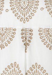 Witte stof met ingewikkelde goudkleurige borduursels met bloem- en druppelpatronen, die fijne details en textuur tonen.