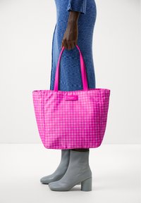 Borsa a spalla imbottita rosa con un motivo a pallini circolari, manici corti e un'etichetta con logo. Indossata con stivali alla caviglia grigi chiari con tacco.