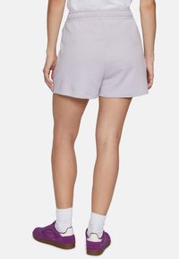 Shorts in lavanda di cotone con vita elastica, caratterizzati da una consistenza liscia e un orlo pulito, abbinati a sneakers viola e calzini bianchi.