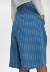 Kék farmer sort fehér függőleges csíkokkal. Magas derekú, oldalsó zsebekkel és hemzsebeléssel rendelkezik. Anyaga sima, enyhén elasztikus.