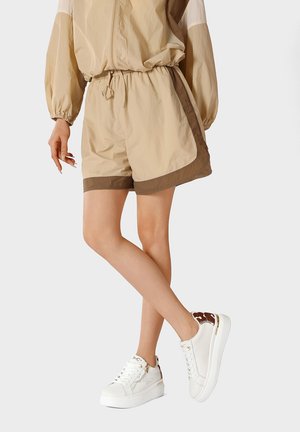 Persona che indossa pantaloncini beige e marroni con una giacca abbinata e sneakers platform bianche con dettagli marroni.