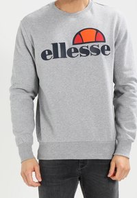 Szara bluza wykonana z miękkiego materiału, z wyraźnym czarno-pomarańczowym logo "ellesse" na wysokości klatki piersiowej. Długie rękawy, dekolt typu crew neck.