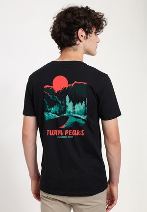 Black cotton t-shirt featuring a vibrant graphic of mountains, trees, and a red sun. Text reads "TWIN PEAKS" with population details below.