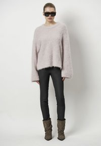 Roze fluffy trui met brede mouwen, gecombineerd met zwarte strakke broeken en bruine slungelige enkellaarsjes. Zonnebril maakt de look compleet.