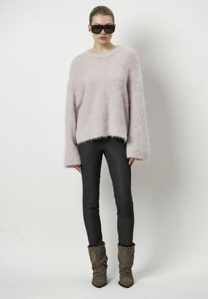 Roze fluffy trui met brede mouwen, gecombineerd met zwarte strakke broeken en bruine slungelige enkellaarsjes. Zonnebril maakt de look compleet.