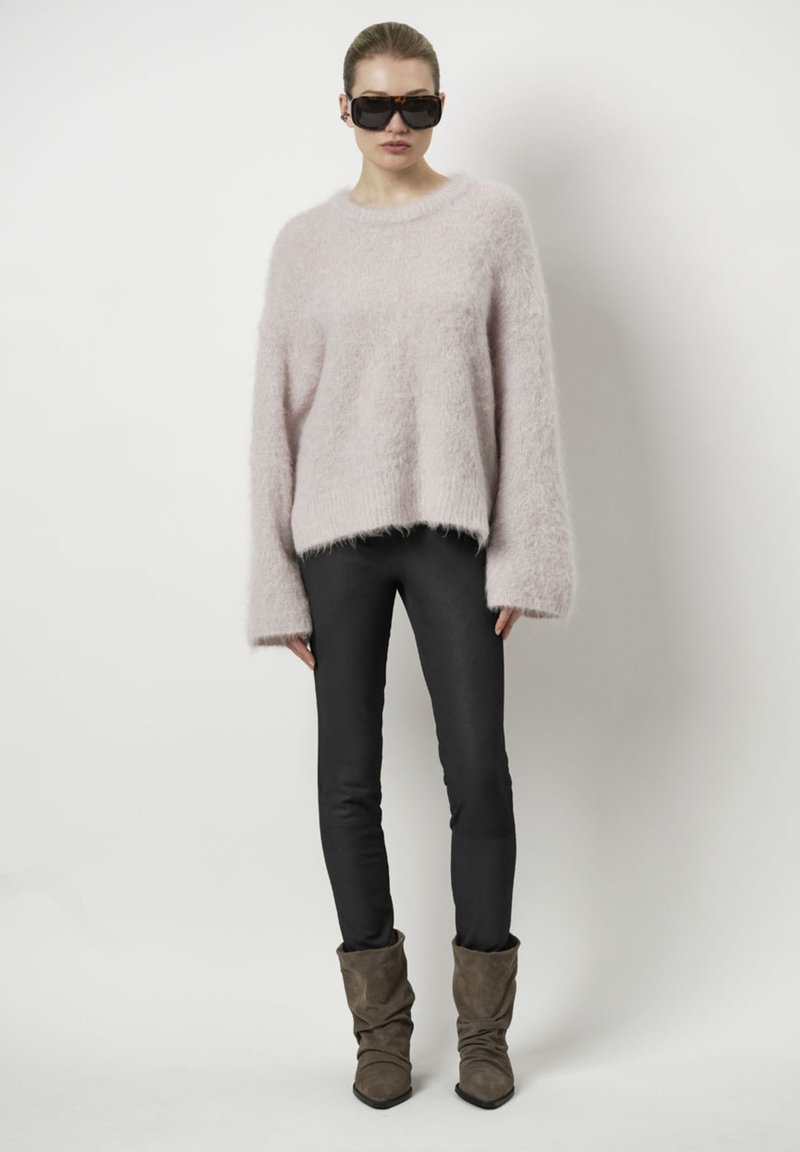 Roze fluffy trui met brede mouwen, gecombineerd met zwarte strakke broeken en bruine slungelige enkellaarsjes. Zonnebril maakt de look compleet.