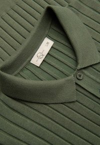 Polo verde a maglia costina con colletto piegato, un bottone e etichetta del marchio visibile all'interno della scollatura.