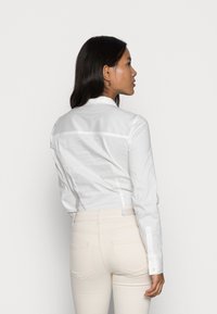 Witte button-up shirt van gladde stof, met een gestructureerde kraag en lange mouwen, gecombineerd met lichtbeige slim-fit jeans.