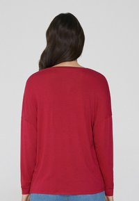 Rotes Langarm-Oberteil mit lockerer Passform, Rundhalsausschnitt und überschnittenen Schultern, aus glattem Stoff. Rückansicht vor einem schlichten Hintergrund.
