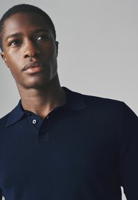 Navyblaues gestricktes Poloshirt mit Kragen, ausgestattet mit einer Drei-Knopf-Leiste und strukturiertem Stoff. Glattes, figurnahes Design ohne Muster.