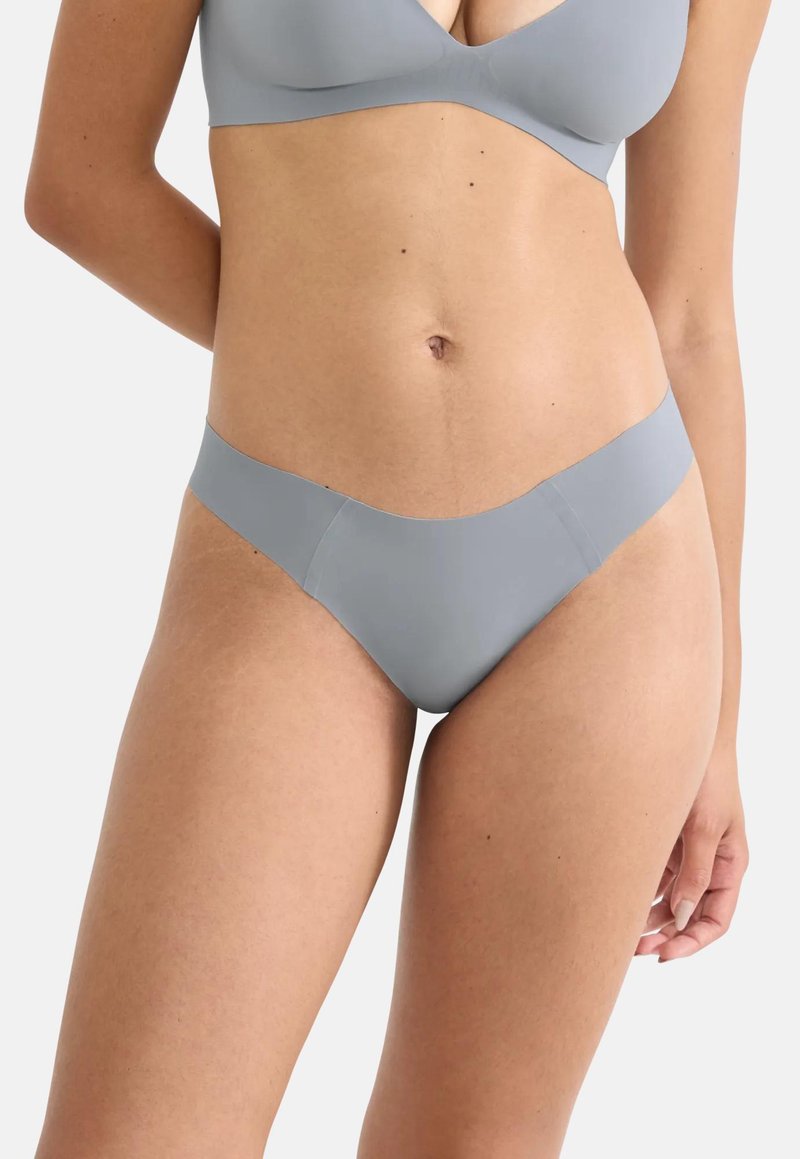 Γυναίκα που φοράει ένα ανοιχτό γκρι seamless σουτιέν και ταιριαστό bikini-style εσώρουχο σε λευκό φόντο.