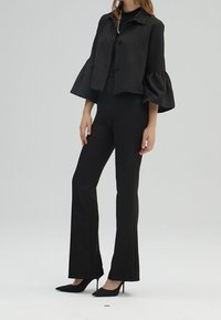 Svart ensemble med en kort jacka med utsvängda ärmar och en åtsittande topp, kombinerat med utsvängda byxor och spetsiga svarta klackar.