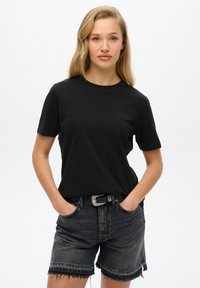 Zwarte katoenen T-shirt met korte mouwen, ronde hals, subtiele branding, gecombineerd met donkere denim shorts met een gefranje zoom en een riem.